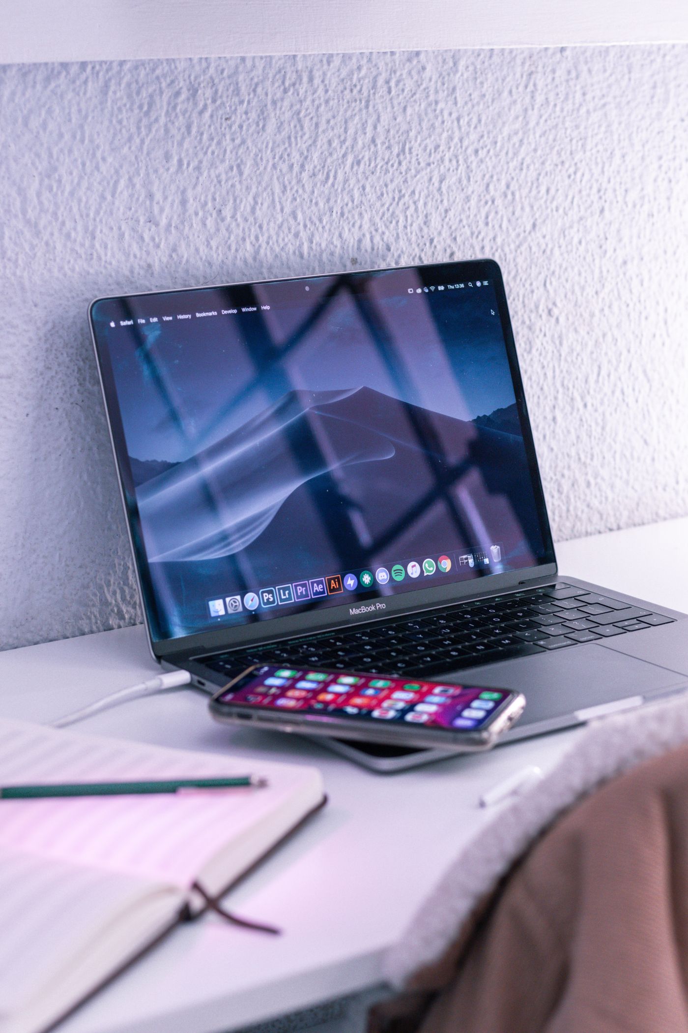 A laptop and smartphone on a desk beside a notebook