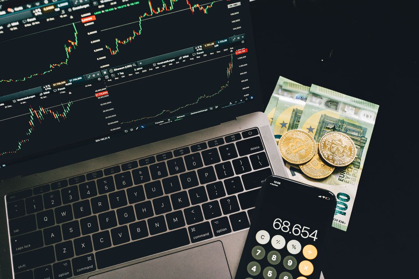 Laptop with financial charts, a phone calculator and decorative Bitcoin coins