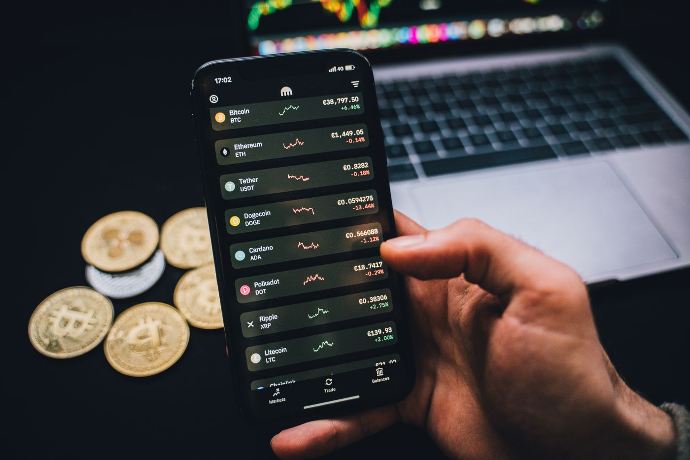 Person comparing cryptocurrency information on a smartphone beside a laptop
