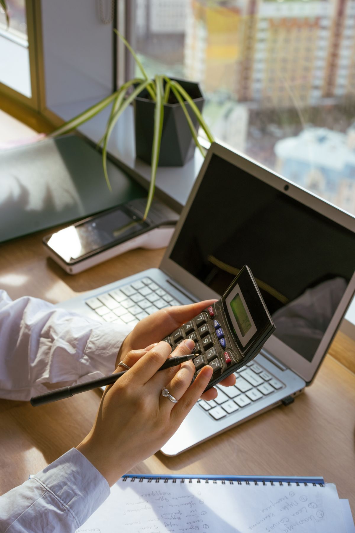 Hands using a calculator beside a laptop and notebook