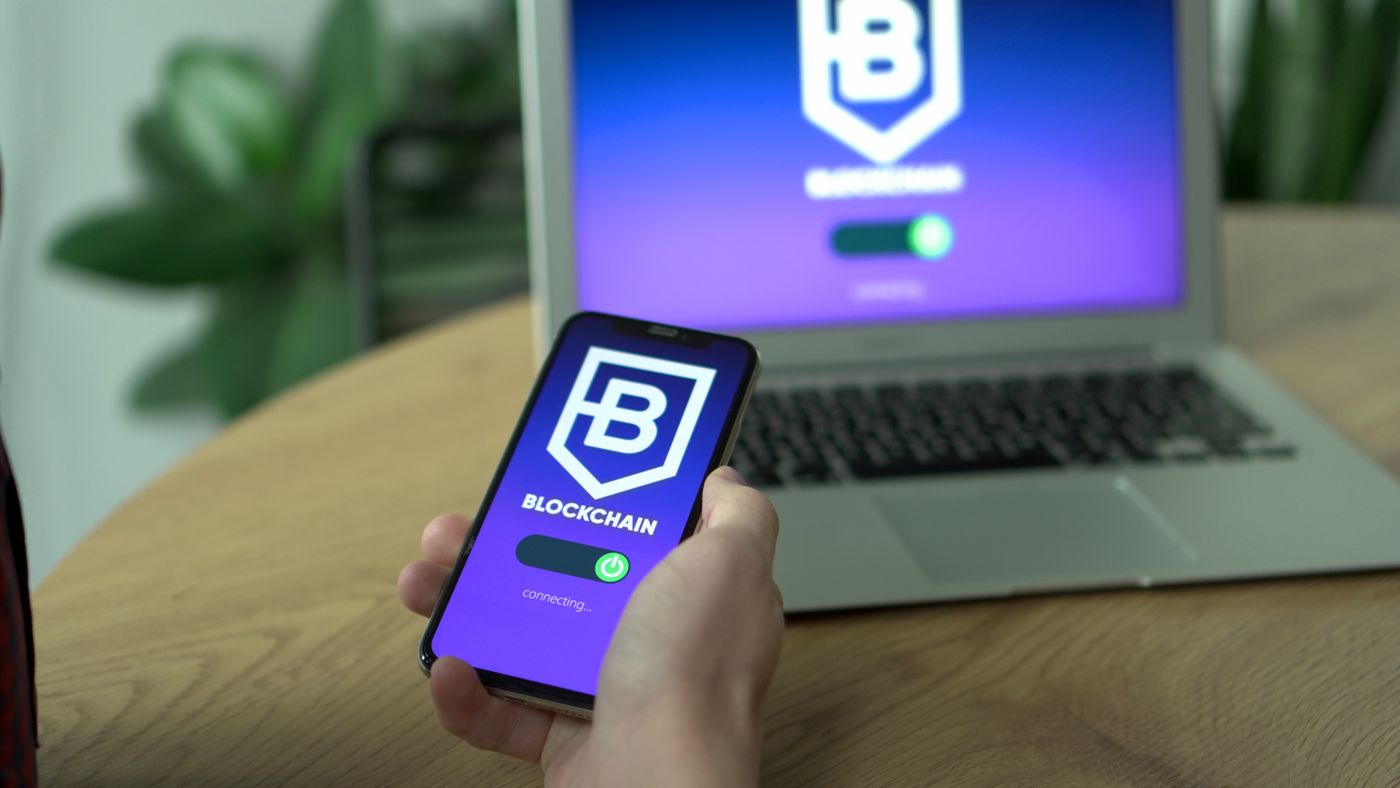 Person holding a smartphone displaying a blockchain app beside a laptop