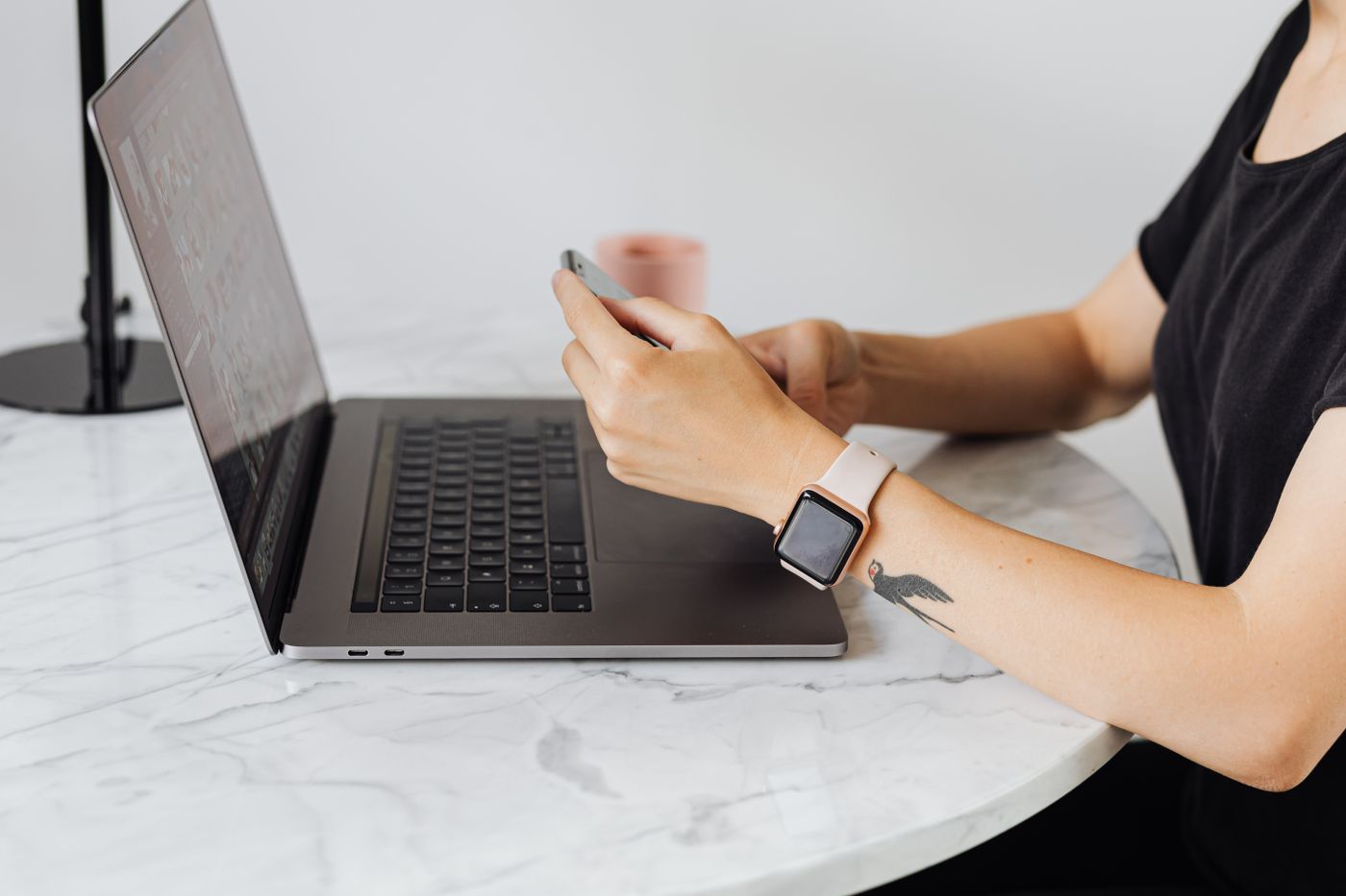A person using a smartphone beside an open laptop at a desk